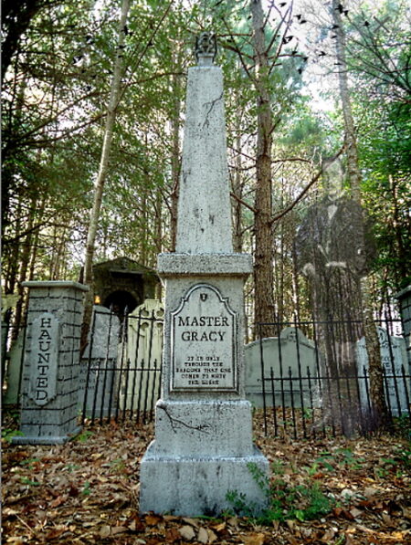 Old tombstone surrounded by trees and iron fence.