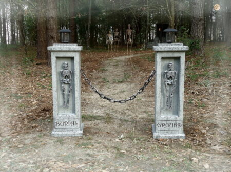 Two stone pillars connected by a chain in a wooded area.