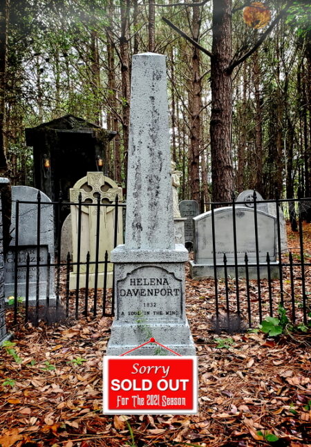 White stone memorial in a forest cemetery with 'Sorry Sold Out' sign.