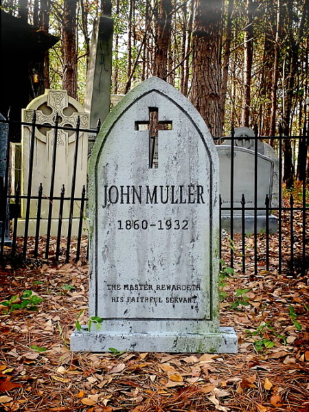 Gravestone of John Muller with a cross in a forest cemetery.