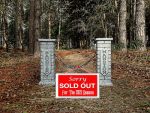 A sold-out sign on a pathway flanked by two white pillars in a forested area.