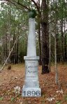 A tall white monument in a wooded area dated 1896.