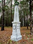 A tall white monument in a wooded area dated 1896.