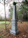 A tall white monument in a wooded area dated 1896.