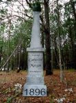 A tall white monument in a wooded area dated 1896.