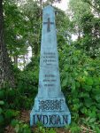 A tall stone monument with a cross, surrounded by greenery.
