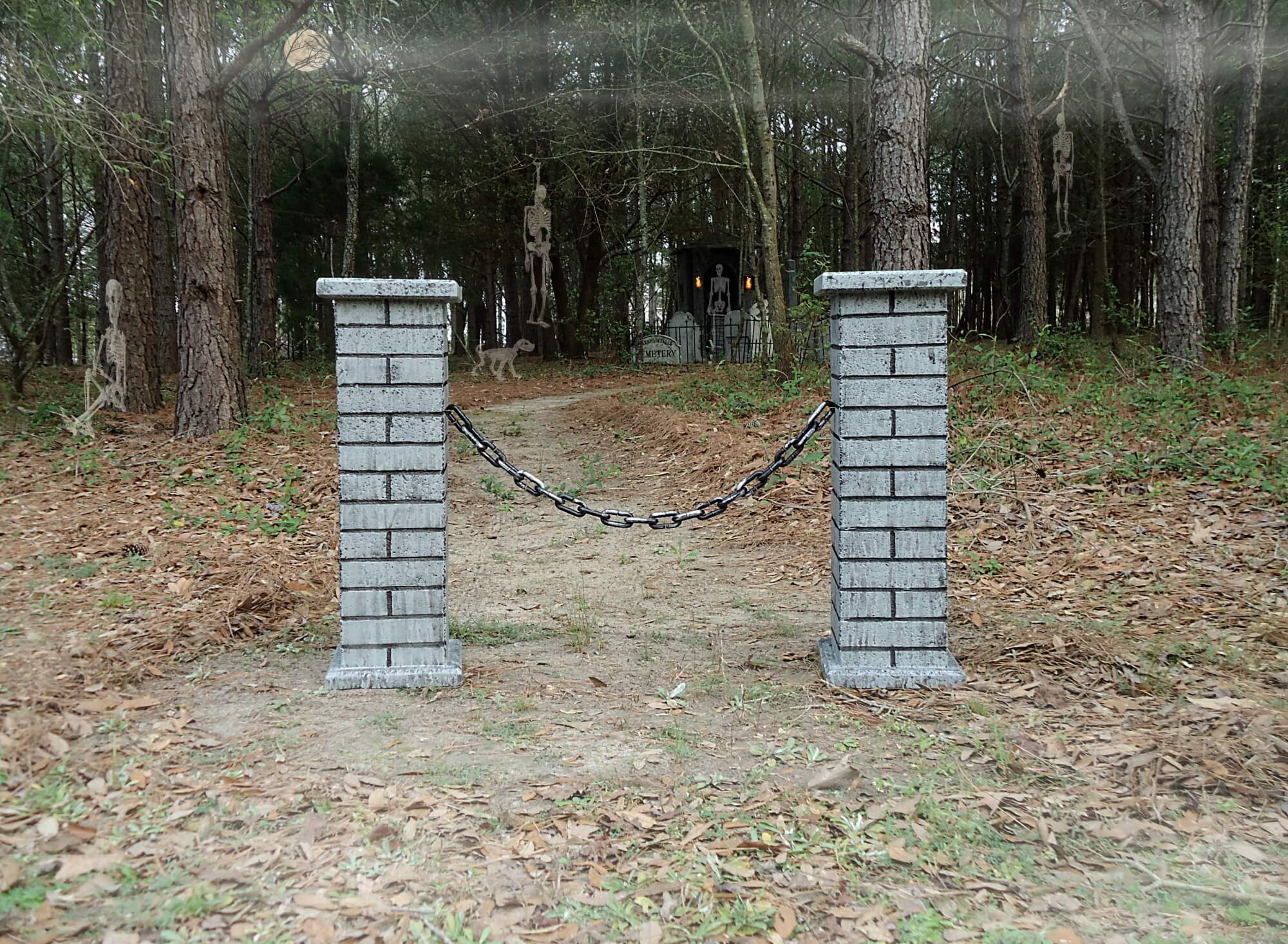 Two brick pillars connected by a black chain in a wooded area. Two brick pillars connected by a black chain in a wooded area.