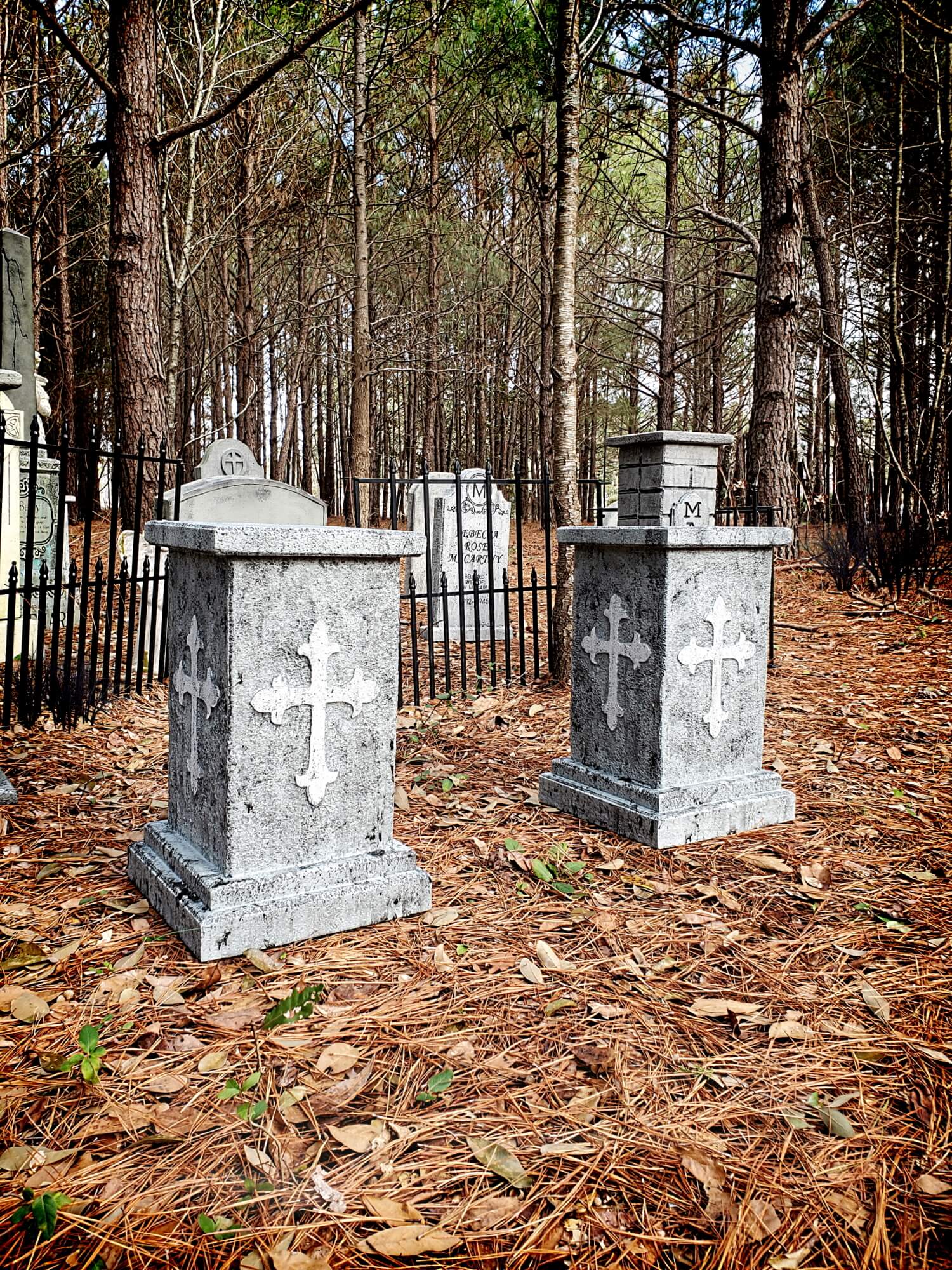 Two stone crosses stand in a wooded cemetery area. Two stone crosses stand in a wooded cemetery area.