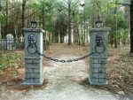 Gated private property entrance with warning signs in a wooded area.