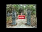 Gated private property entrance with warning signs in a wooded area.