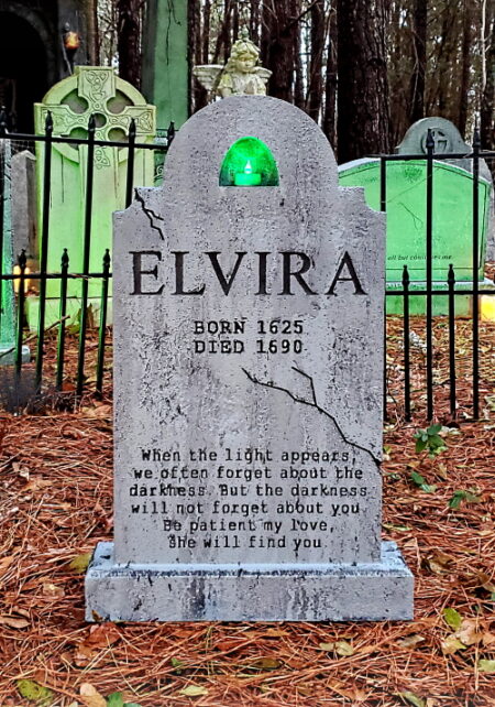 A tombstone for Elvira in a forested area with iron fencing.