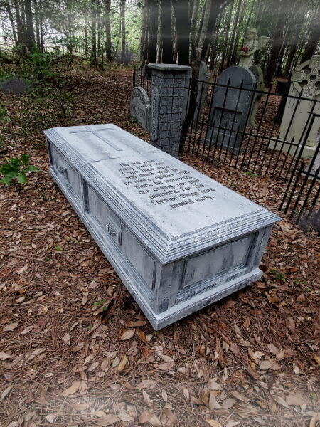 Stone tomb in a wooded cemetery area with engraved text.