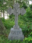 Stone cross gravestone with the name Galen in a green cemetery.