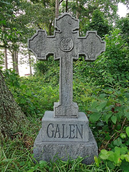 Stone cross gravestone with the name Galen in a green cemetery.