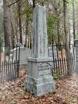 White stone memorial in a forest cemetery with ‘Sorry Sold Out’ sign.