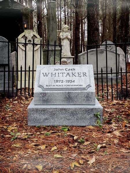 A gravestone for William in a fenced area covered with autumn leaves.