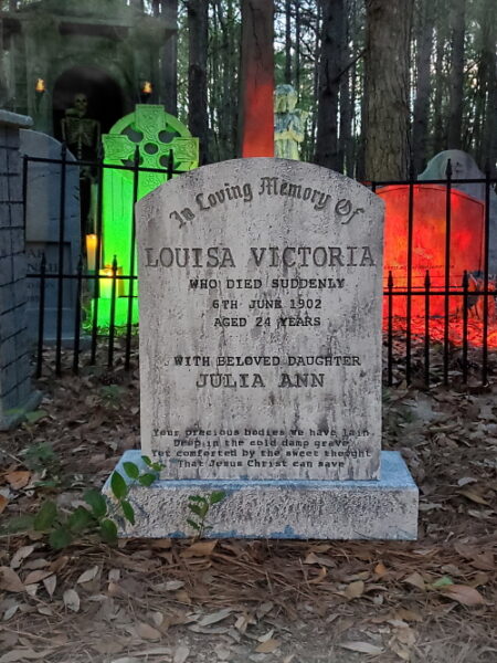 Old gravestone in a forested area with inscriptions and a green lantern.