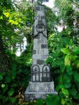 A tall stone monument with engraved inscriptions surrounded by greenery.