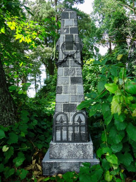 A tall stone monument with engraved inscriptions surrounded by greenery.