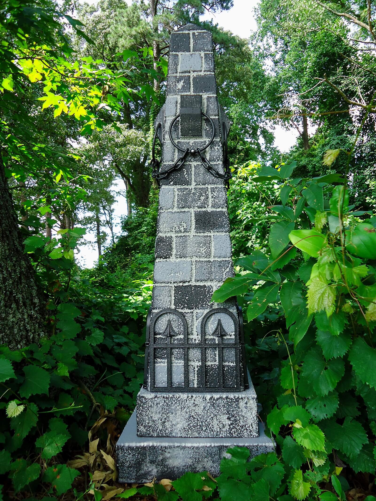 A tall stone monument with engraved inscriptions surrounded by greenery. A tall stone monument with engraved inscriptions surrounded by greenery.