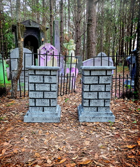 Two stone pillar decorations with purple bows in a wooded area.