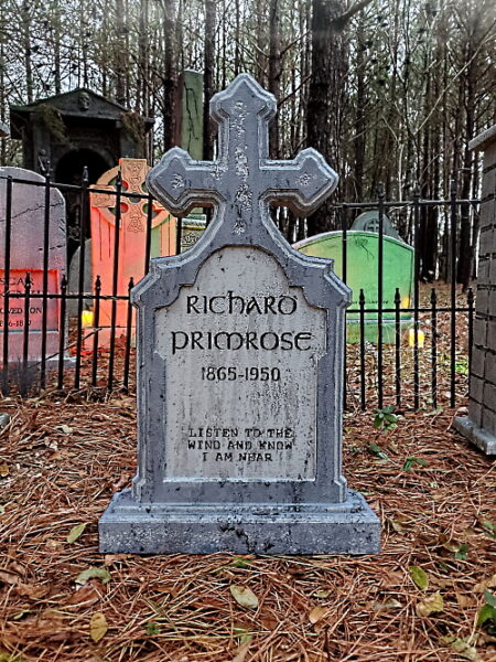 A weathered stone grave marker in a wooded cemetery.