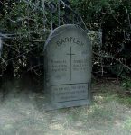 A weathered gravestone with inscriptions in a foggy, wooded area.