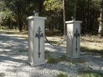 Two stone pillars with metal crosses in a wooded area.
