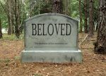 A gravestone engraved with ‘BELOVED’ in a forest setting.