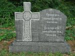 A stone Celtic cross gravestone in a grassy area.