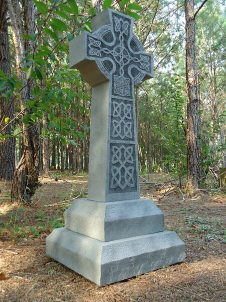 Stone Celtic cross monument in a wooded area.