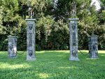 Four decorative stone pillars with intricate designs stand on a grassy lawn.