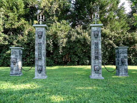 Four decorative stone pillars with intricate designs stand on a grassy lawn.