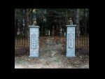 Two stone pillars at a forest entrance with a pathway beyond.
