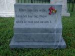 A gray granite tombstone with an inscription and a small flower decoration.