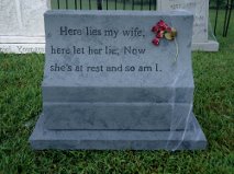 A gray granite tombstone with an inscription and a small flower decoration.
