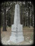 A stone monument with inscriptions stands in a forested area.