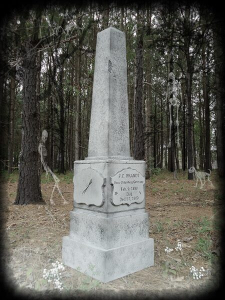 A stone monument with inscriptions stands in a forested area.
