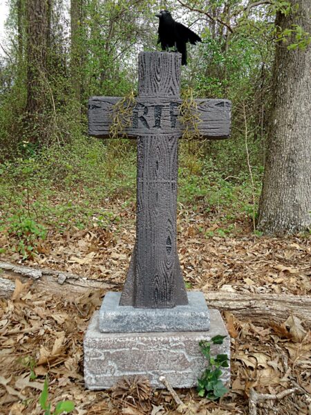 Old wooden grave marker with a black crow statue on top in a forest.